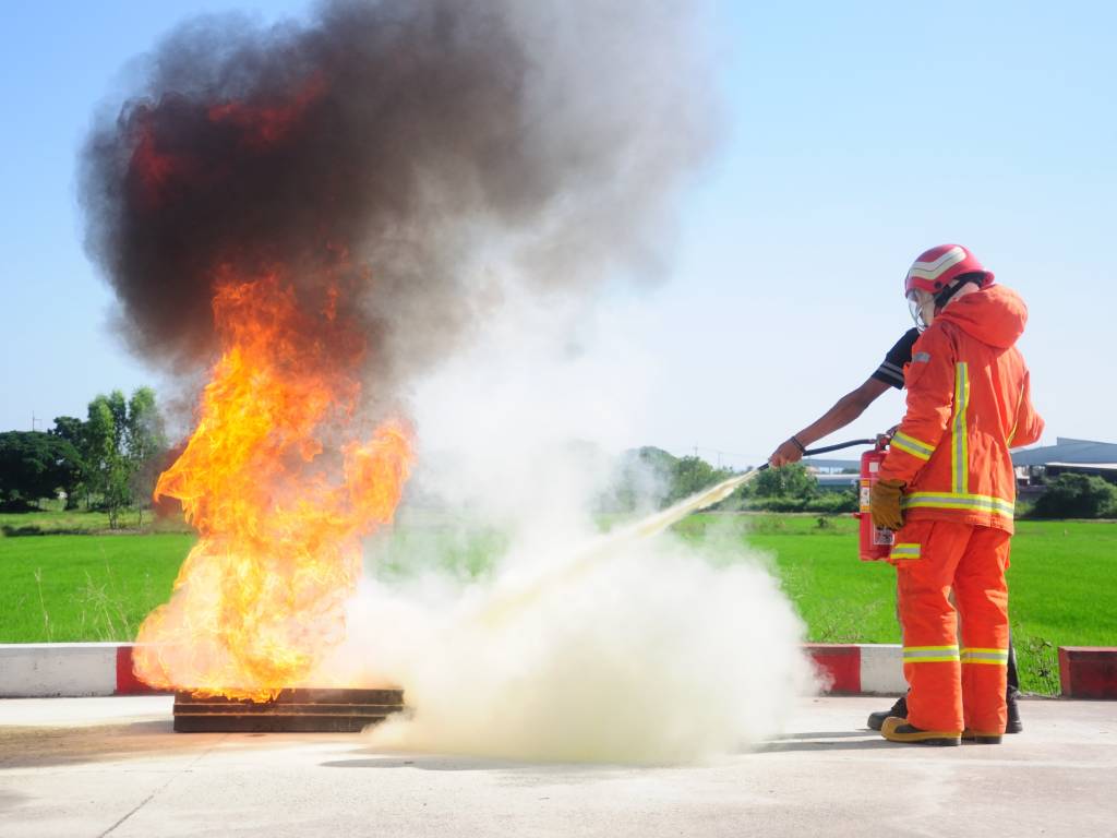 Feuerwehrtrainer löscht brennende Feuerwanne mit Feuerlöscher während einer Brandschutzhelfer Ausbildung